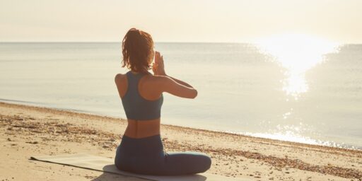 Wellnessurlaub - Frau meditiert am Strand