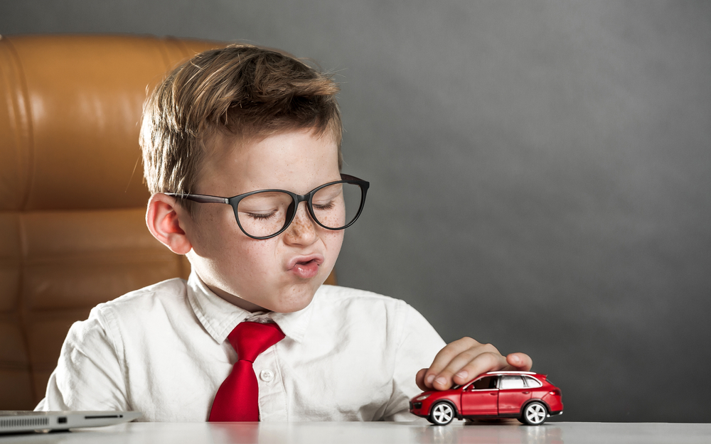 Kleiner Junge in Business-Aufzug spielt mit einem Modellauto